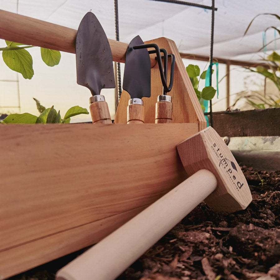 Gardening tools on a wooden holder with plants in the background