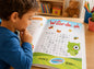 Child reading a 'Woordsoek' book with colorful illustrations on a wooden table.