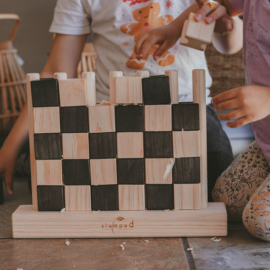 Children playing with a wooden block puzzle resembling a castle, branded 'stumpad'.