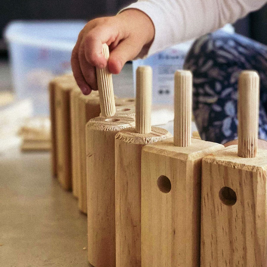 Wooden pegs being inserted into wooden blocks with holes, likely part of a educational or construction toy.